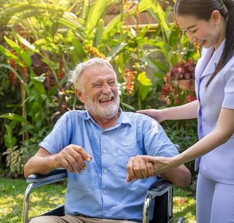 A carer sharing a joke with a man in a wheelchair outdoors